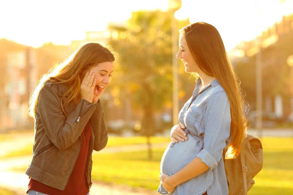 Amazed girl looking at her pregnant friend belly